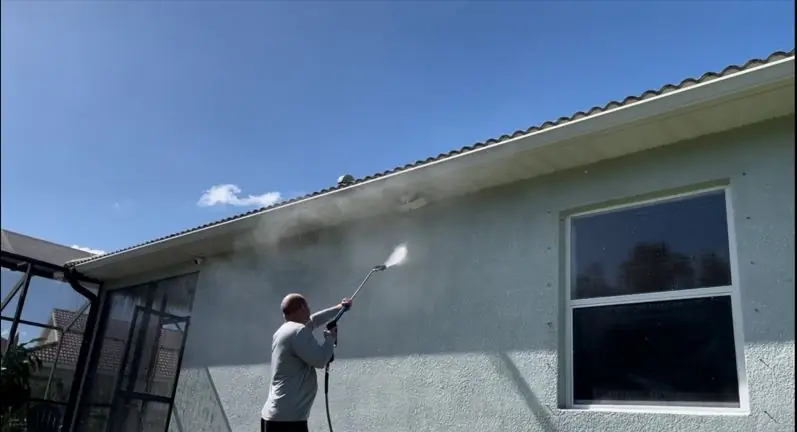 Crew member rinsing mildew from a stucco wall beside a screened lanai