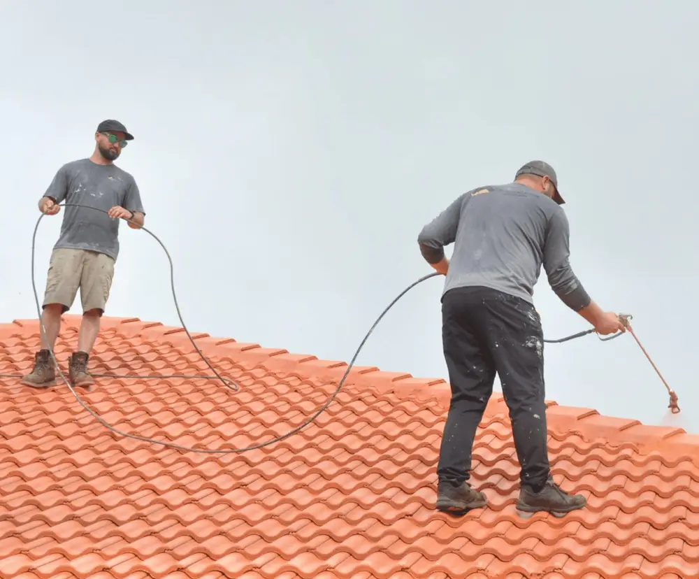 Two roof coating technicians spraying color coating on a terracotta concrete tile roof